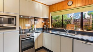 A modern kitchen with stainless steel appliances, wooden cabinets, and a window with a view of greenery.