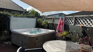 A hot tub, a table, and chairs in a backyard with a wooden fence and potted plants.