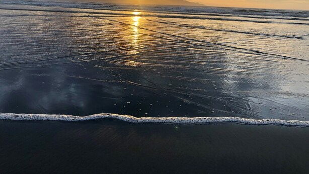 A beach with waves and a sunset.