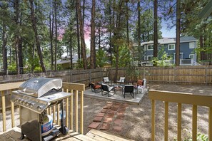 Une terrasse extérieure équipée d’un barbecue, d’un espace salon et offrant une vue sur une zone boisée.
