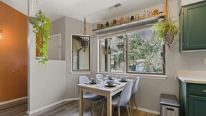 A dining area with a table set for four, a window with a view of trees, and hanging plants. - *Home Gym* A/C* Fenced-in Yard (Flagstaff)