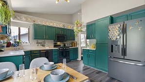 A modern kitchen with teal cabinets, stainless steel appliances, and a dining area with a wooden table set for four. - *Home Gym* A/C* Fenced-in Yard (Flagstaff)