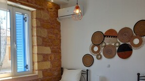 Een slaapkamer met twee bedden, een stenen muur, een raam met luiken en wanddecoraties van geweven materiaal.