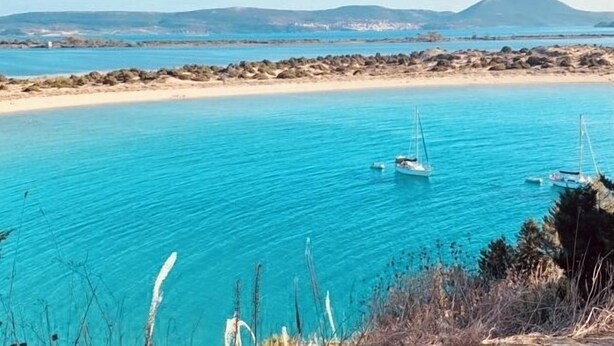 Een uitzicht op de kust met helder turquoise water, een zandstrand en boten.