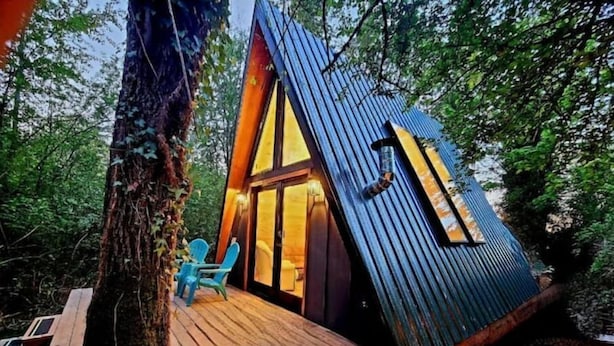 A treehouse with a wooden deck, a small seating area, and a large window.