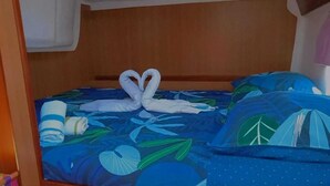 Ein Bett mit blauer, floraler Bettdecke und Kissen, ein hölzernes Kopfteil und eine Handtuch-Anordnung in Herzform.