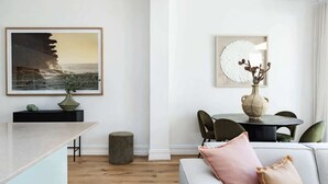 A modern living room with a dining area, a large framed painting, a vase with dried flowers, and a round table. - Charming Tropical Bondi Retreat (Bondi Beach)