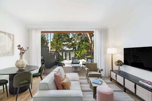 A modern living room with a sofa, chairs, a dining table, and a TV. - Charming Tropical Bondi Retreat (Bondi Beach)