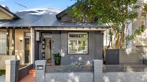 A residential house with a grey facade, a metal roof, and a small front garden. - Charming Tropical Bondi Retreat (Bondi Beach)