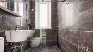 A modern bathroom with a glass shower enclosure, a white sink, and a marble-tiled floor. - Charming Tropical Bondi Retreat (Bondi Beach)