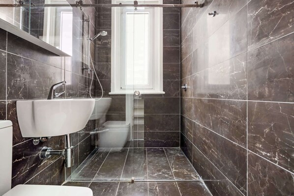 A modern bathroom with a glass shower enclosure, a white sink, and a marble-tiled floor. - Charming Tropical Bondi Retreat (Bondi Beach)