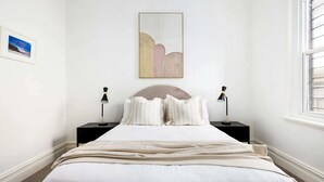 A bedroom with a bed, two bedside tables, a nightstand, a window, and a wall-mounted artwork. - Charming Tropical Bondi Retreat (Bondi Beach)