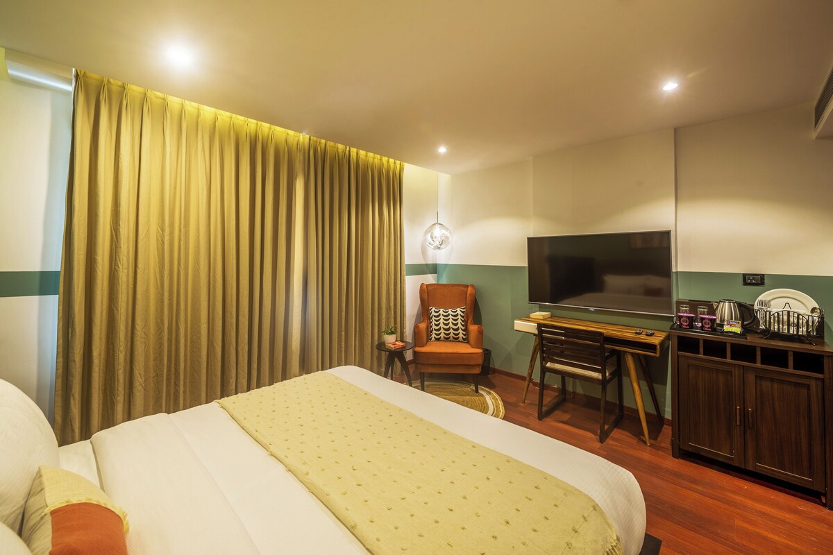 A hotel room with a large bed, a desk with a chair, a television, and a wardrobe.