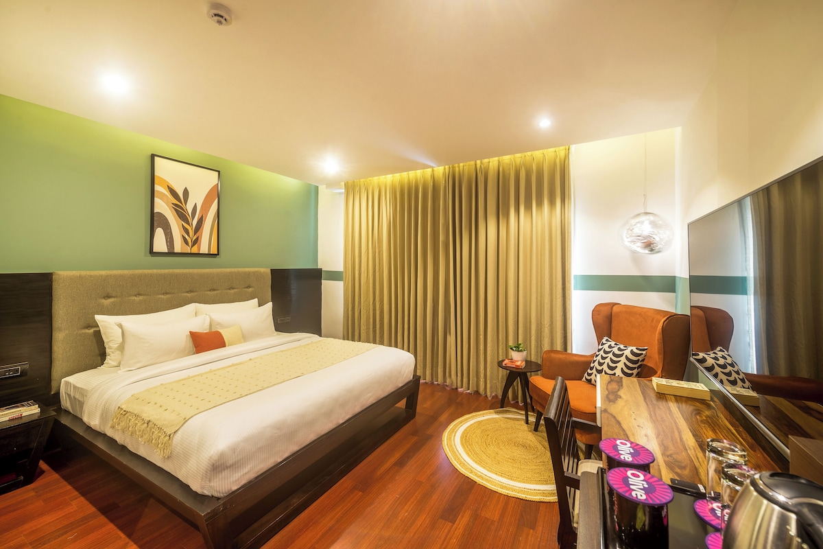 A hotel room with a bed, a small table with a bottle, a chair, and a TV.
