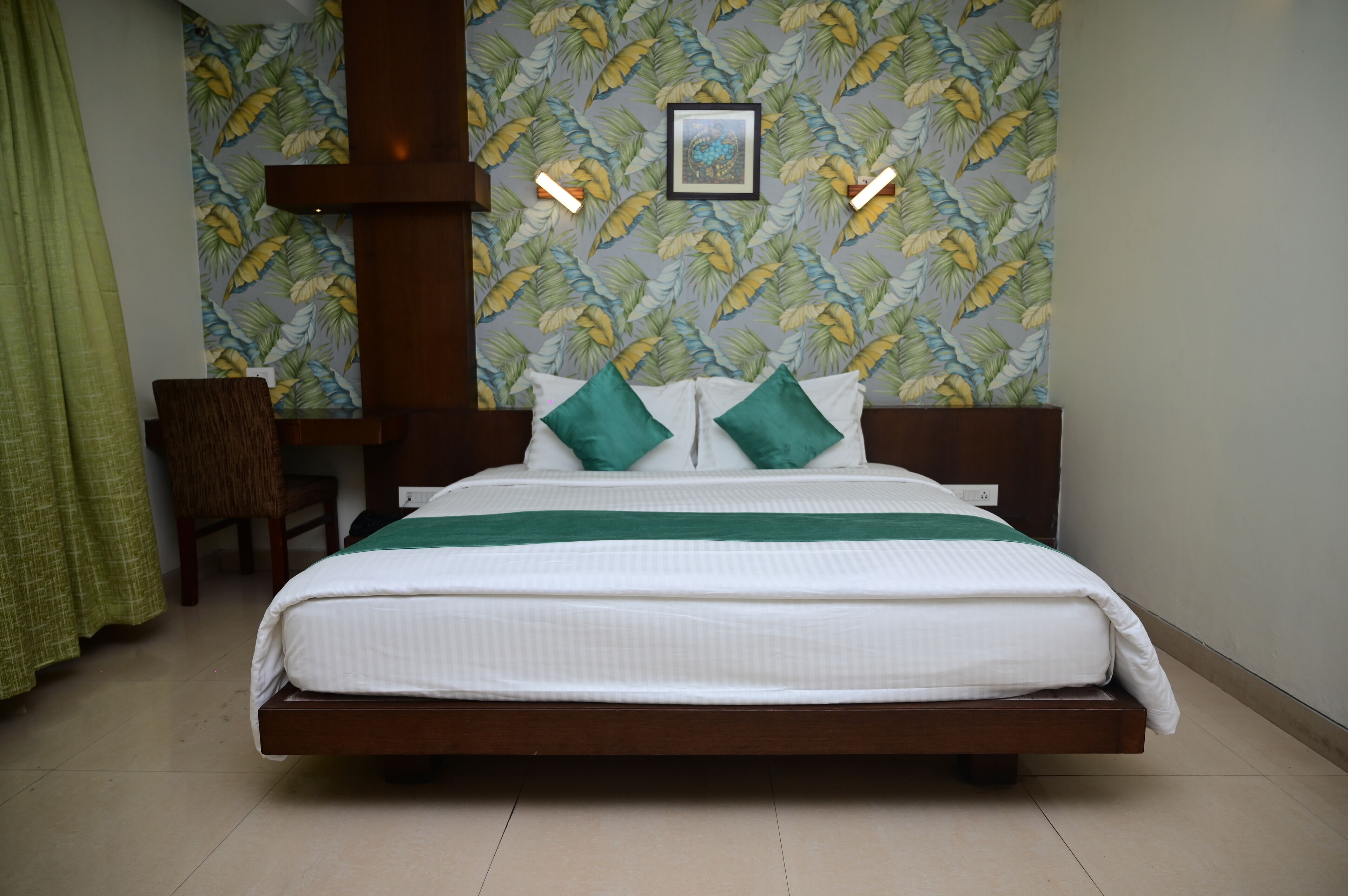 A neatly made bed with a green and white bedspread, two green pillows, and a framed picture on the wall above.