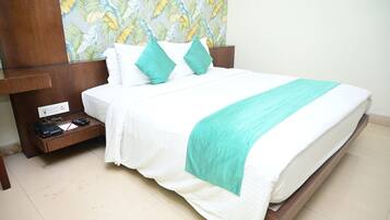 A neatly made bed with white bedding and teal accents, a wooden nightstand with a printer, and a wall with a tropical leaf pattern.