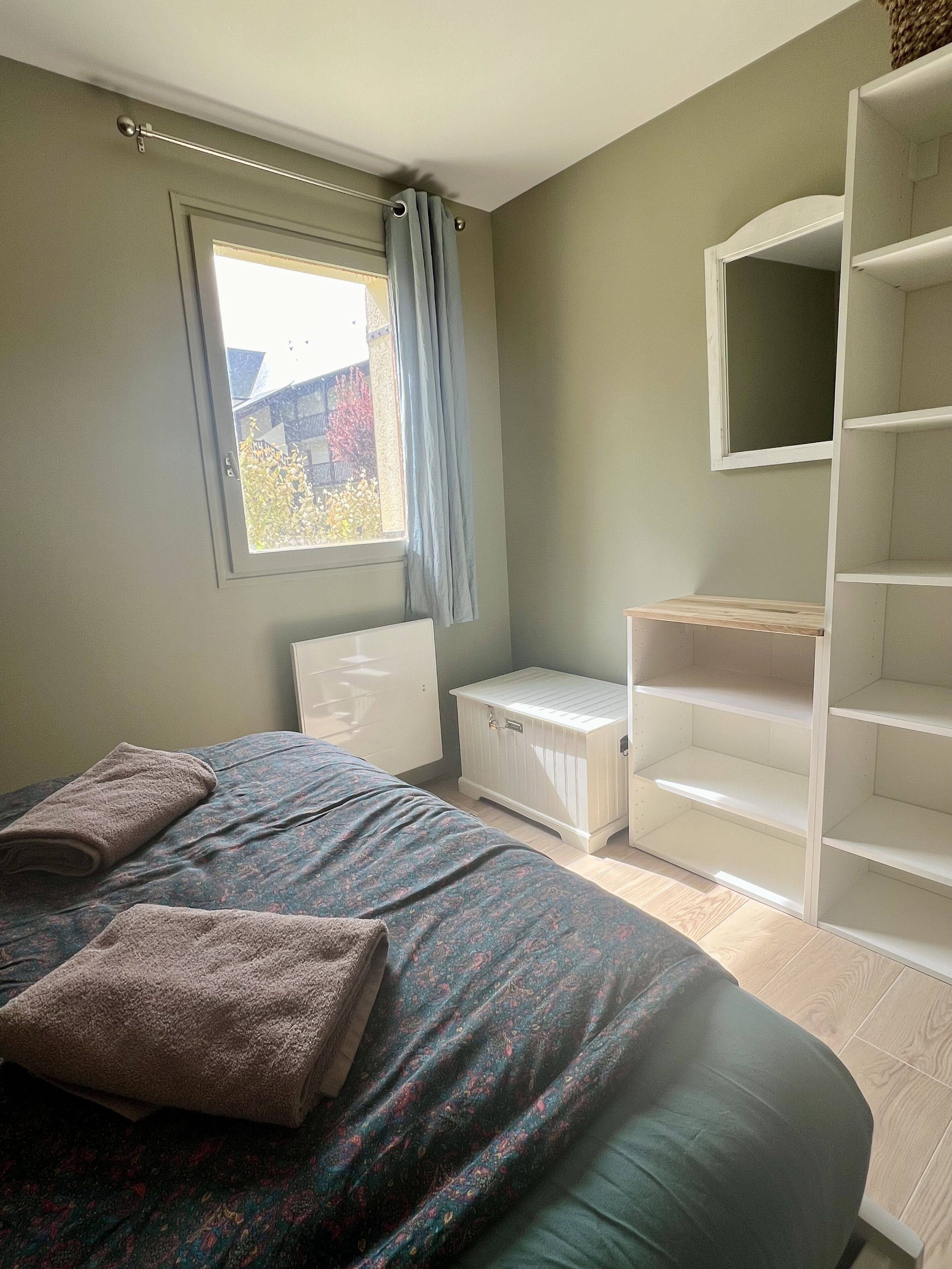Ett sovrum med en säng, ett fönster med gardiner, en vit garderob och en inbyggd hyllsektion.