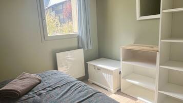 Ett sovrum med en säng, ett fönster med gardiner, en vit garderob och en inbyggd hyllsektion.
