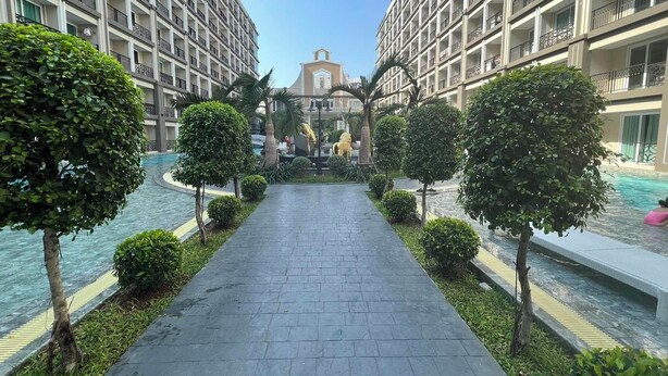 A pathway leading to a building with a central courtyard, surrounded by trees and a pool.