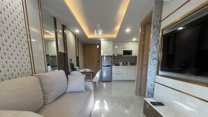 A modern living room with a sofa, a TV mounted on the wall, and a kitchen in the background.