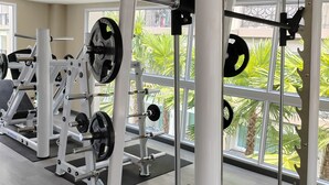 A gym with weightlifting equipment, large windows, and a view of greenery outside.