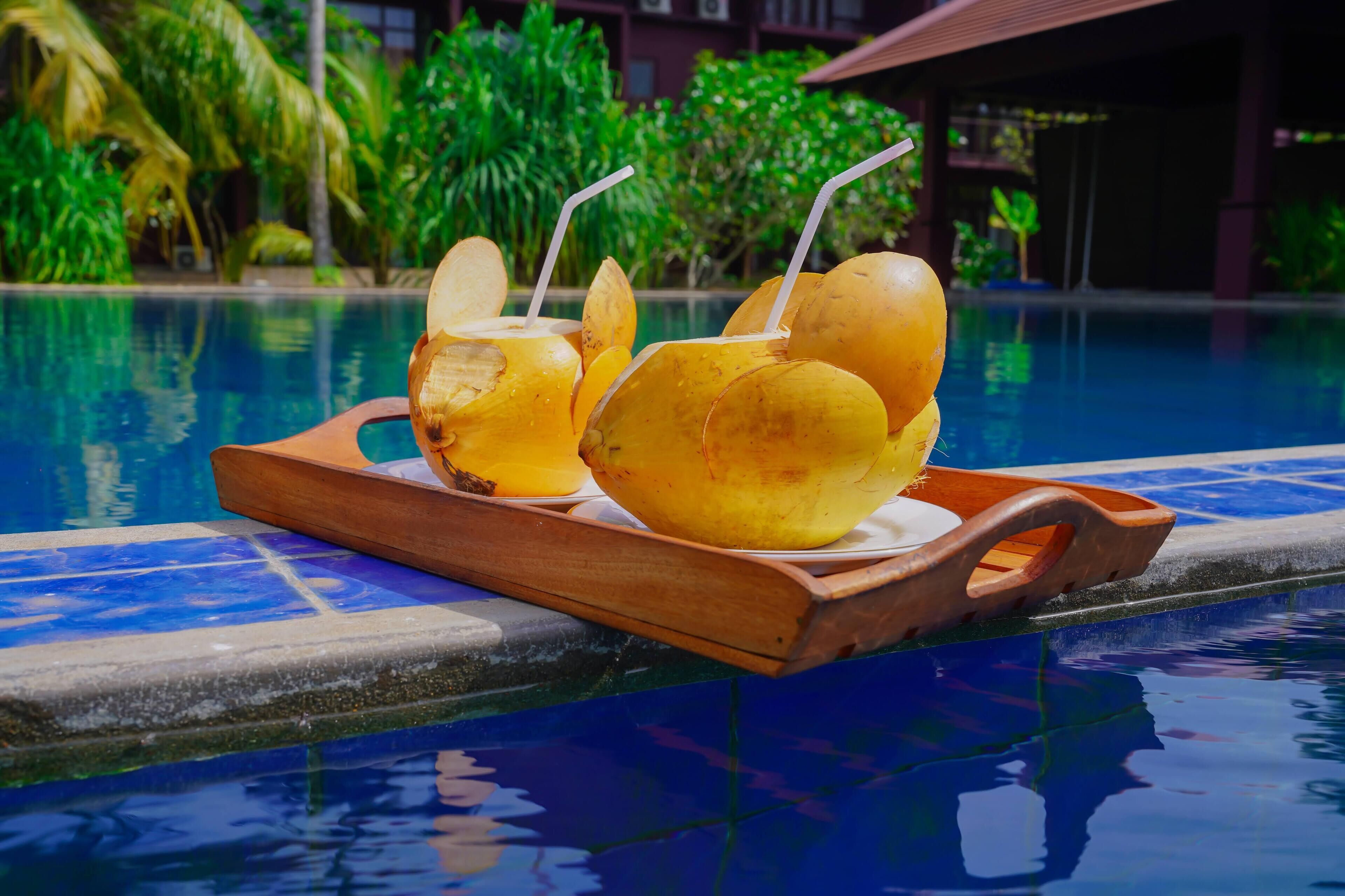 Una bandeja de madera con dos cocos y una bebida junto a la piscina.