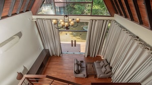 A spacious living area with a high ceiling, a wooden staircase, and a view through large windows.