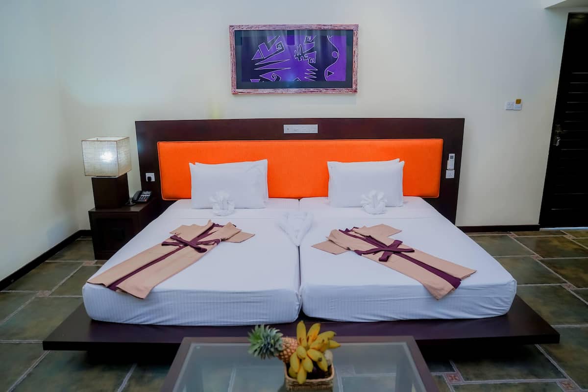 A double bed with an orange headboard, two pillows, and a decorative wall piece above.