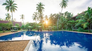A swimming pool with lounge chairs and umbrellas, surrounded by palm trees and a building.