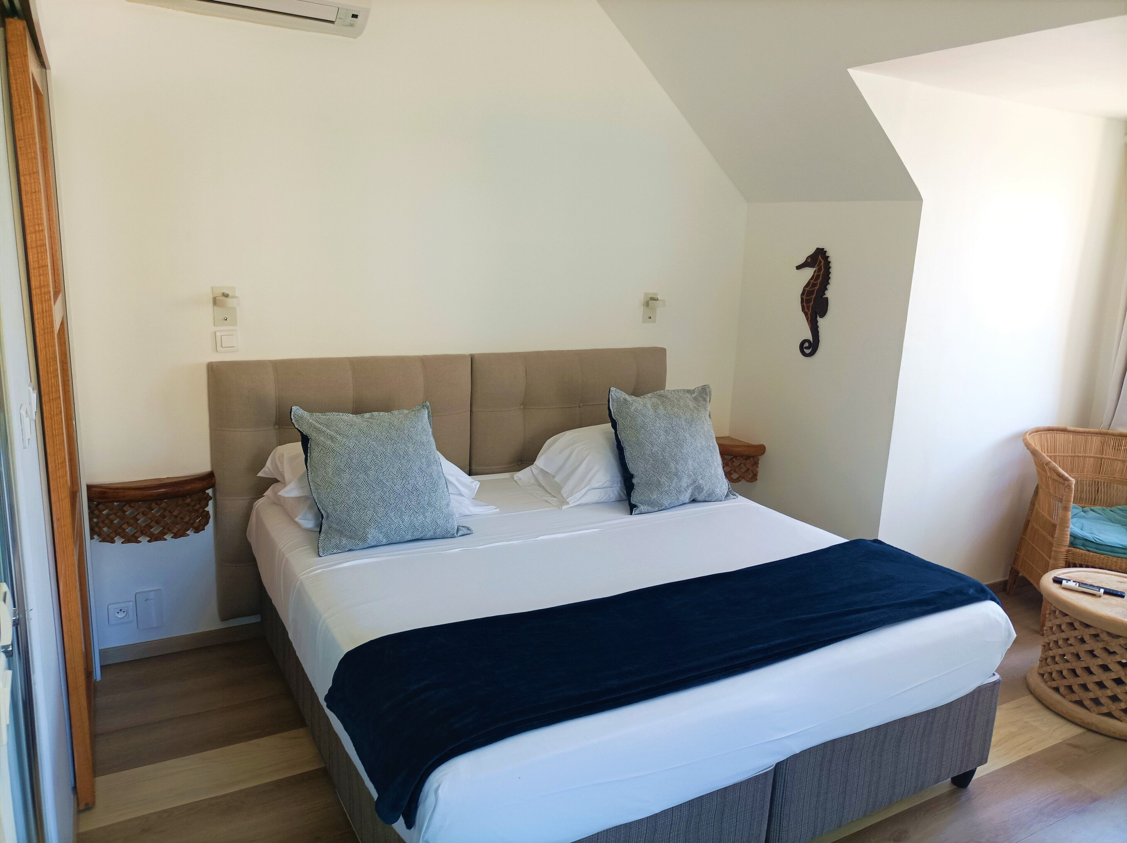 A bedroom with a bed, two pillows, a bedside table, a wall-mounted light, and a decorative wall piece.