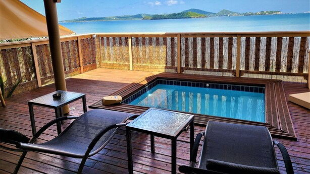 A wooden deck with a pool, lounge chairs, and a table. - Hôtel Hamaha Beach (Mamoudzou)