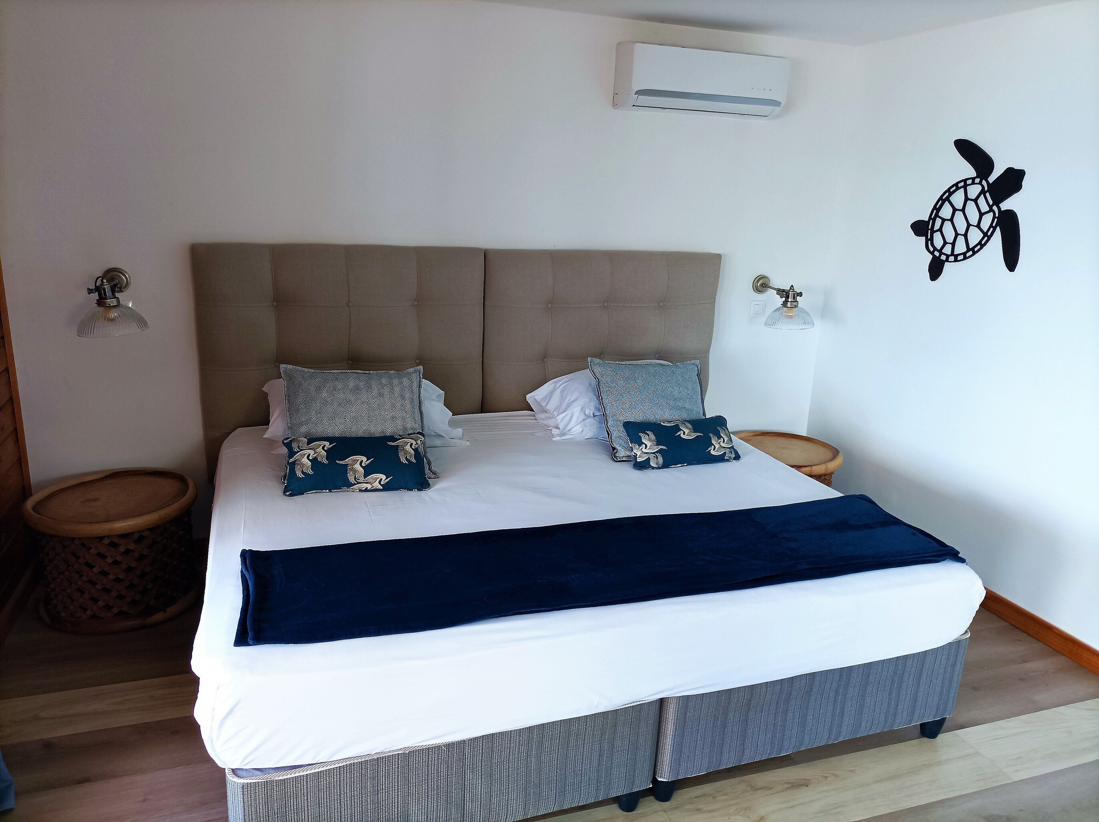 Una cama bien hecha con un edredón azul oscuro, dos almohadas con un estampado de pájaros y un cabecero.