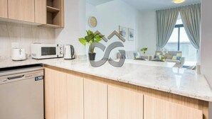 A modern kitchen with wooden cabinets, a microwave, a coffee maker, and a dishwasher. There is a dining area with a sofa and a plant.