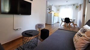 A modern living room with a flat-screen TV, a sofa, a dining area with a table and chairs, and a kitchen in the background. - Holiday House O'Live - private house with a garden few steps from the sea (Marina)
