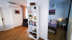 A modern living room with a white bookshelf, a grey sofa, and a wooden floor. - Holiday House O'Live - private house with a garden few steps from the sea (Marina)