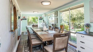 A dining area with a long wooden table, cushioned chairs, and a view of the garden through large windows. - Secluded in the Heart of Sequim (Sequim)