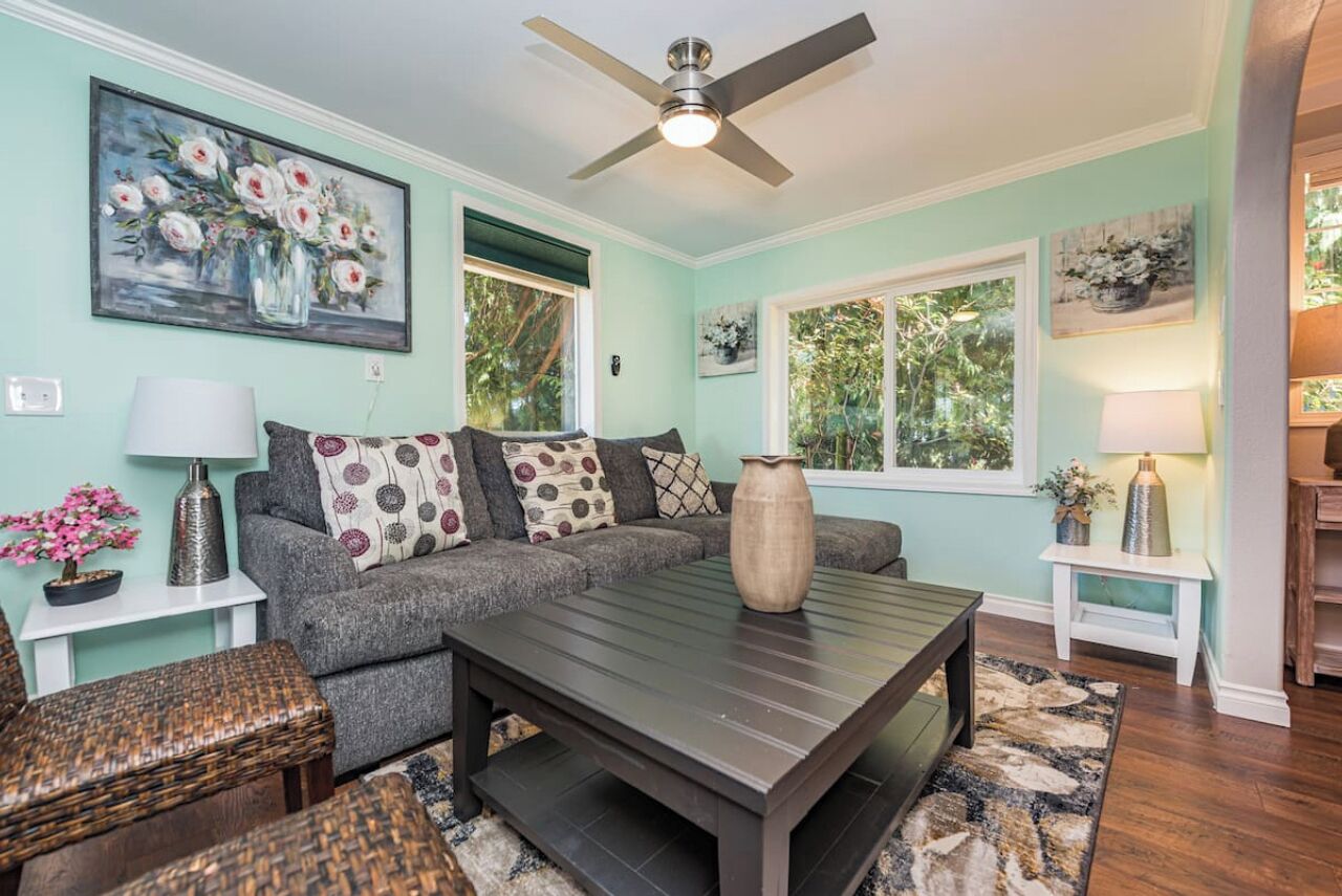 A living room with a sectional sofa, a coffee table, wicker chairs, and a ceiling fan.