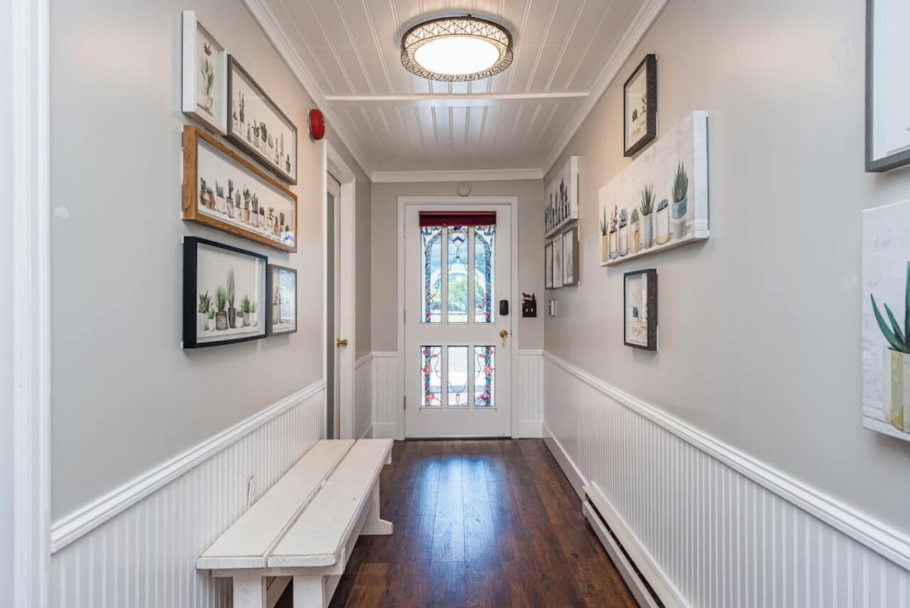 A hallway with framed botanical prints on the walls, a bench, and a door with stained glass.