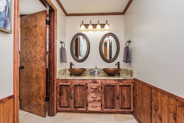 A bathroom with wooden cabinetry, a double sink with copper fixtures, and a vanity mirror.