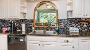 A kitchen with white cabinets, a stainless steel sink, and a mosaic backsplash. - Secluded in the Heart of Sequim (Sequim)