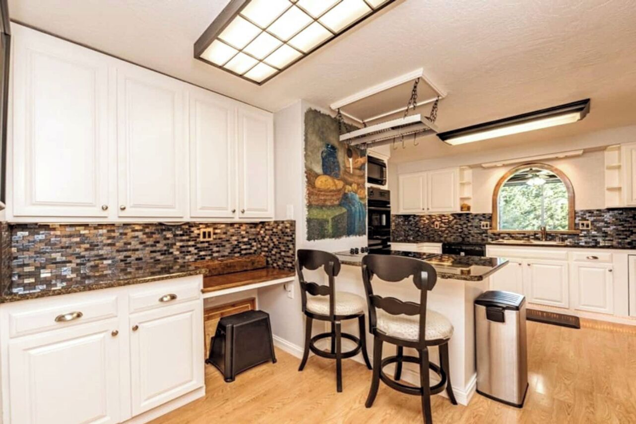 A modern kitchen with white cabinets, a mosaic backsplash, and a central island with bar stools.