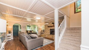 A spacious living room with a grey sofa, wooden flooring, a stone fireplace, and a staircase. - Secluded in the Heart of Sequim (Sequim)