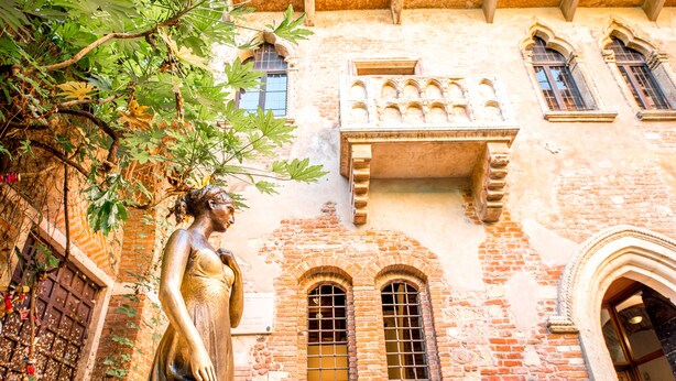 A historic building with a statue, arched windows, and a brick facade.