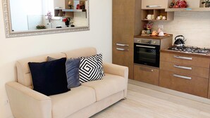 A modern kitchen with a built-in oven, a gas stove, and a microwave. There is a beige sofa with decorative pillows and a large mirror above it.