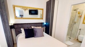A modern bedroom with a large bed, a television above the bed, and a glass shower area.