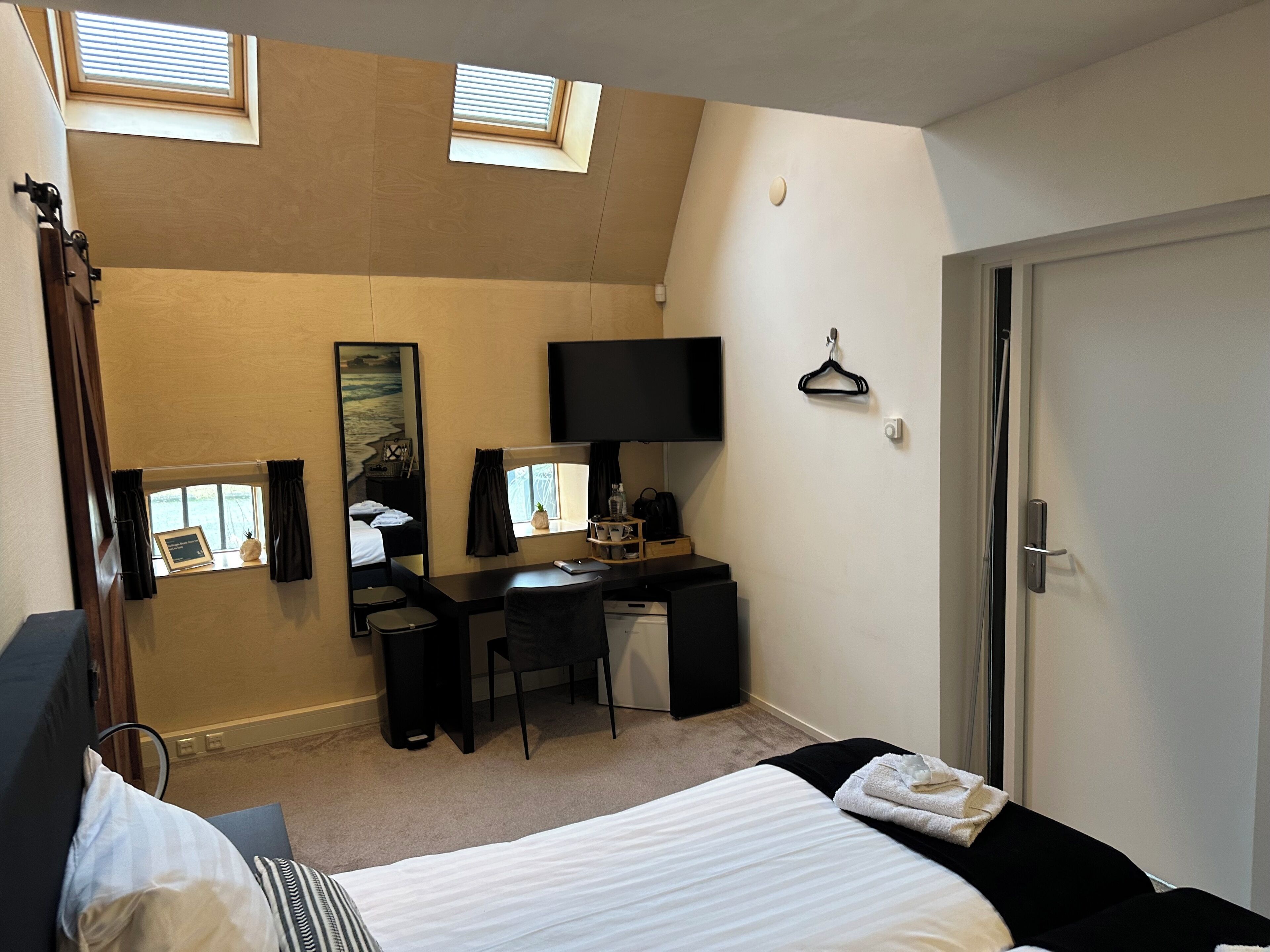 A hotel room with a bed, a desk, a chair, a television, a mirror, and a window with blinds.