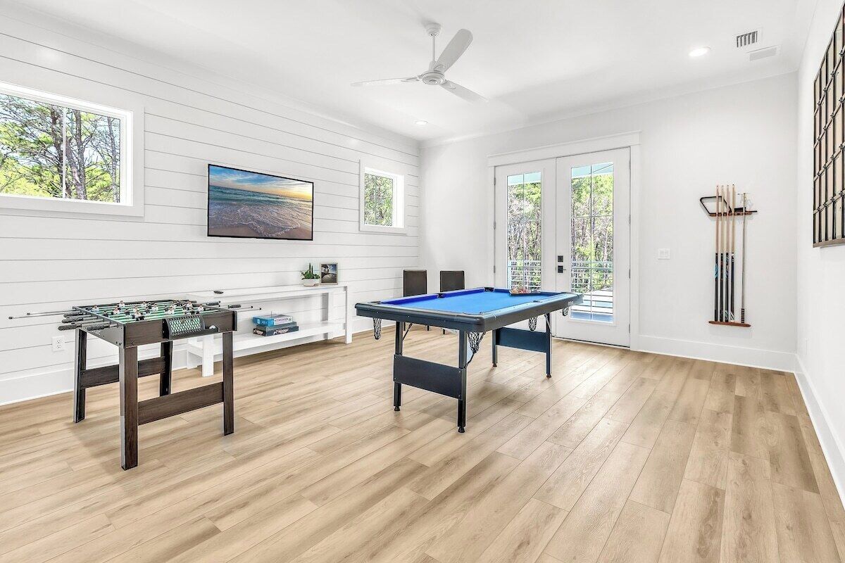 A spacious room with a pool table, a foosball table, and a ceiling fan.