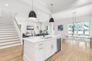A modern kitchen with white cabinetry, a central island with a sink, pendant lighting, and a view of the outside.