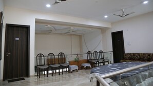Une chambre d’hôtel comprenant un lit, des ventilateurs de plafond, un coin salon avec des fauteuils, une petite table et un panneau décoratif mural.