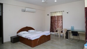 Une chambre à coucher comprenant un lit, un bureau, deux chaises, un climatiseur et un ventilateur de plafond.